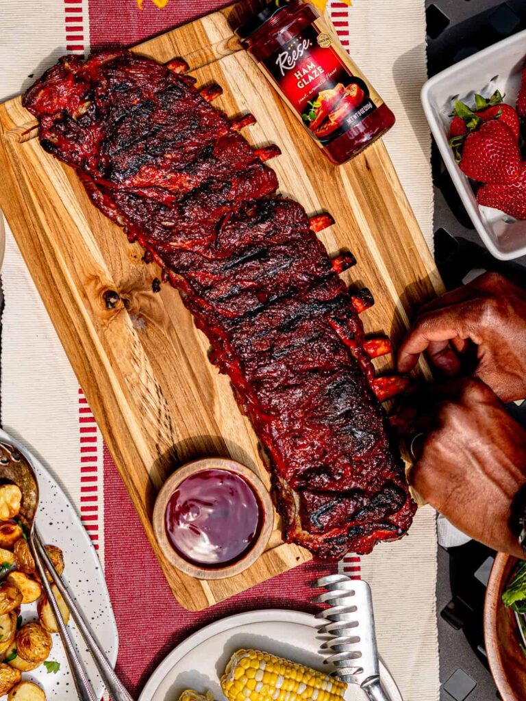 One of our favorite summer recipes, a succulent rack of St. Louis ribs, perfectly glazed with a rich, sticky barbecue sauce, served on a wooden cutting board with a side of pickles and coleslaw.